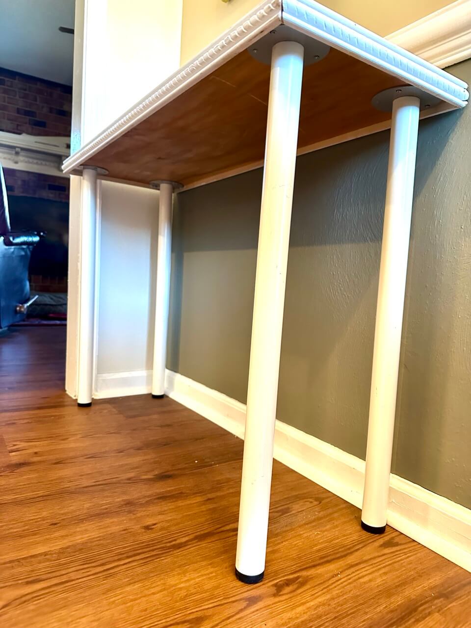 Small wooden table with white legs on a wooden floor against a wall.