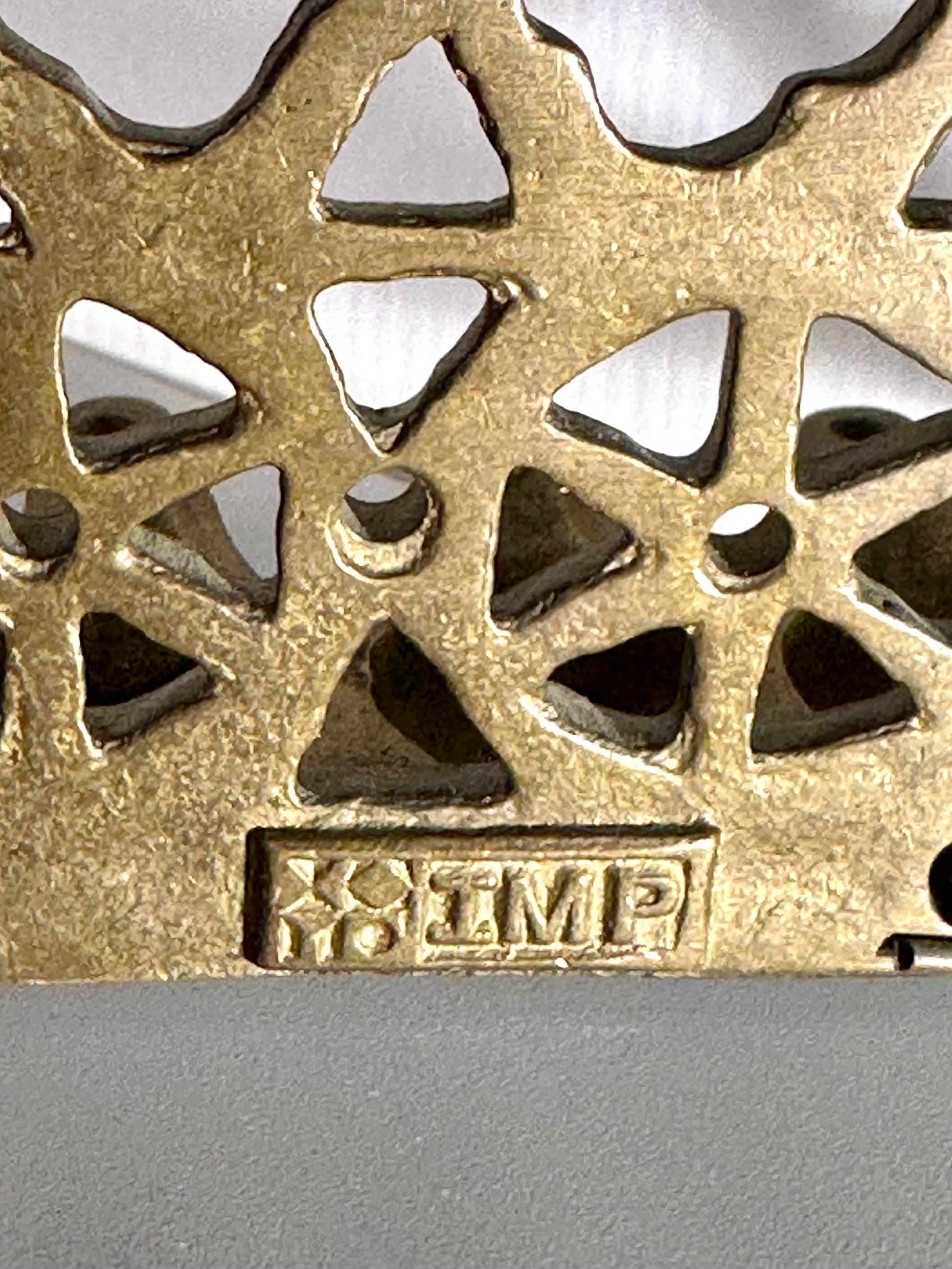 Metallic decorative object with geometric patterns and 'IMP' branding on a gray background