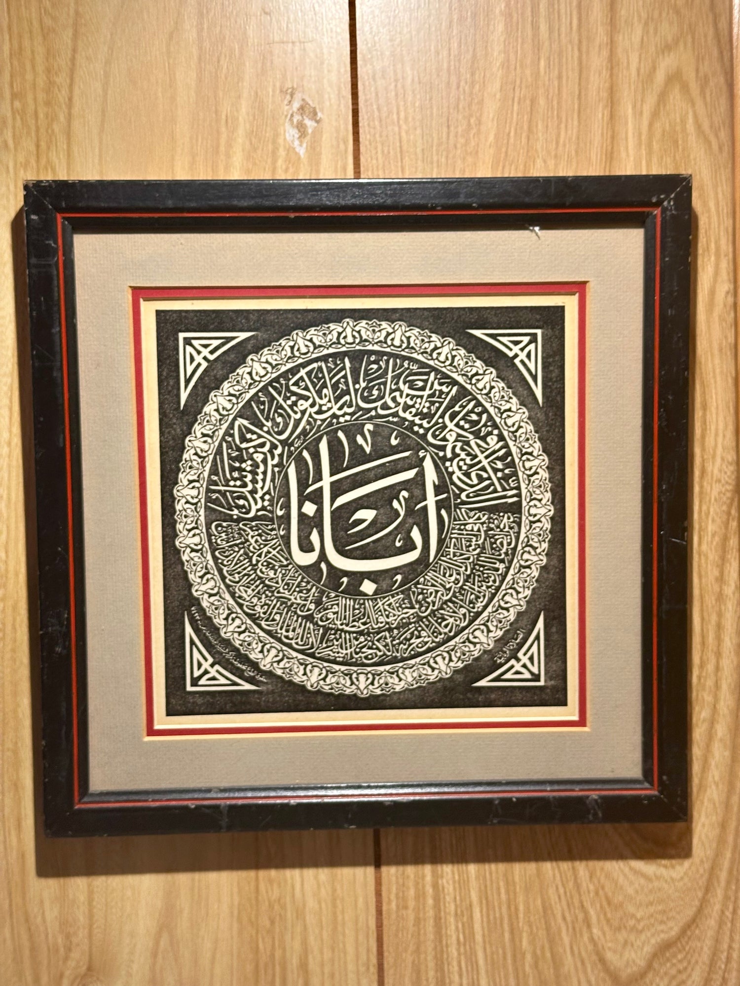 Framed artwork with Arabic calligraphy on a wooden surface
