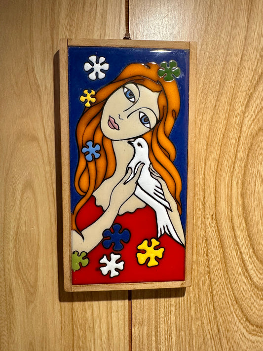Decorative tile with a stylized illustration of a woman holding a dove on a wooden surface.