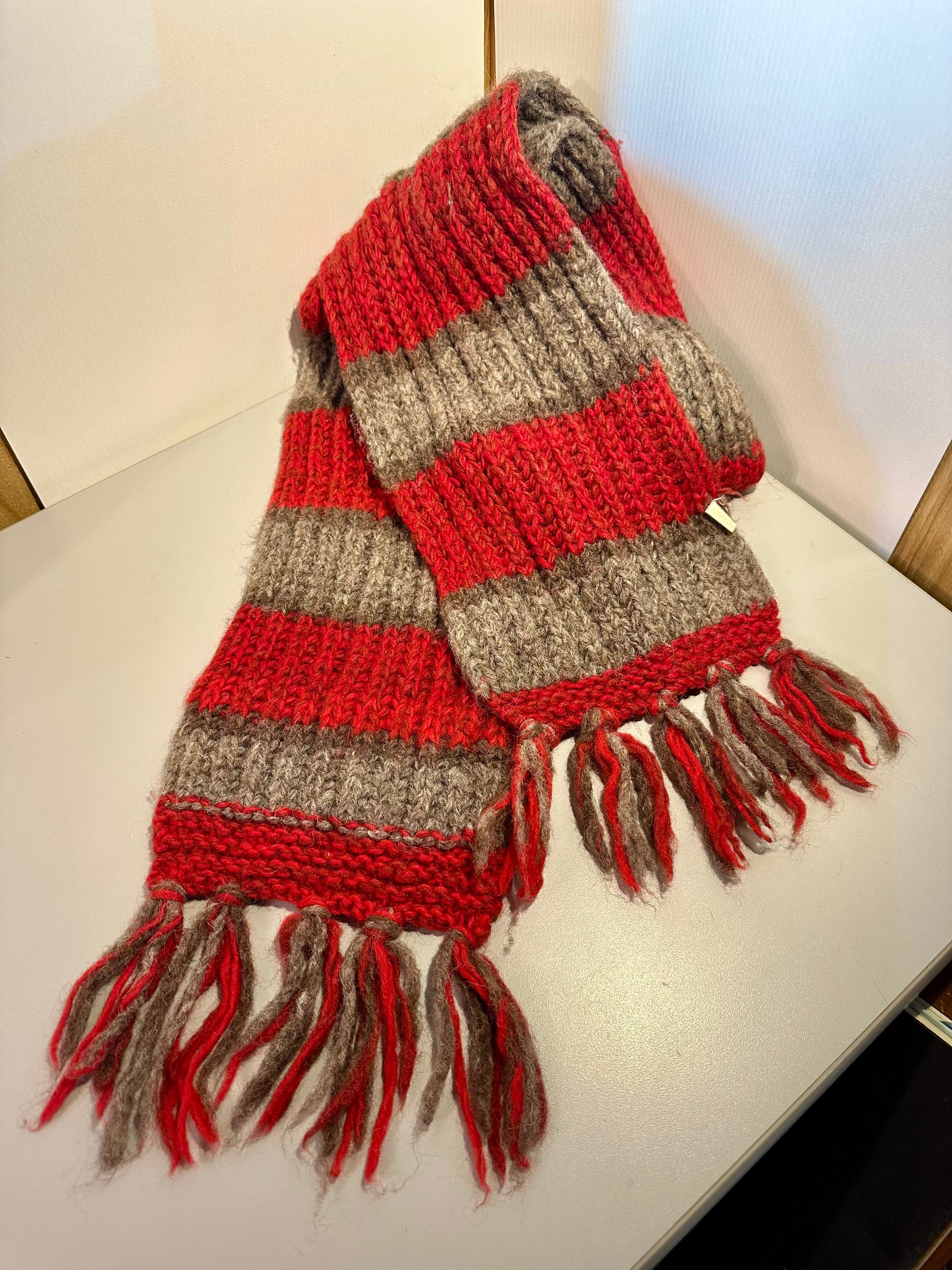 Red and gray striped scarf with tassels on a white surface