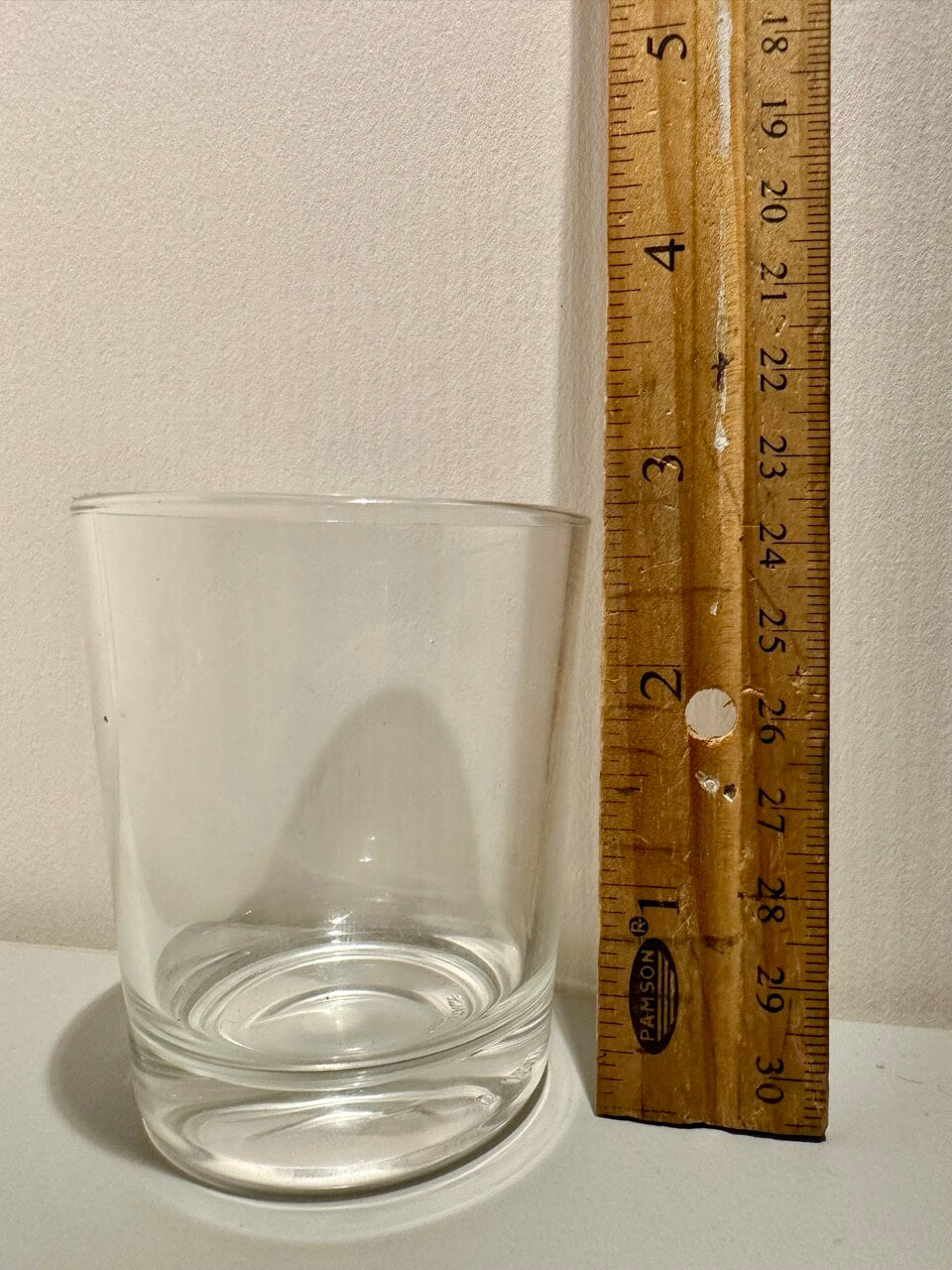 Clear glass tumbler next to a wooden ruler on a white surface