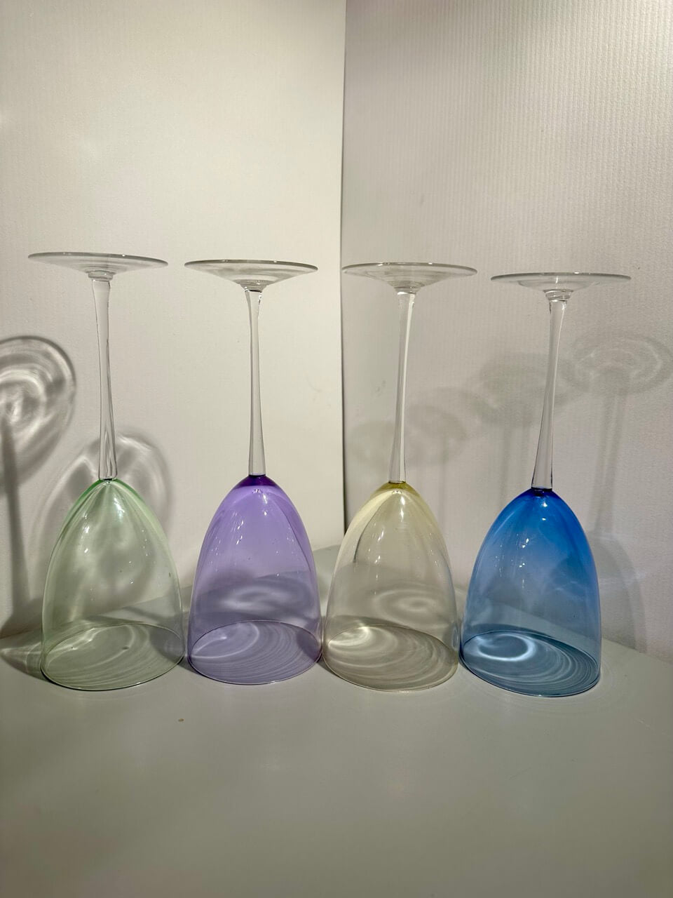 Four colorful wine glasses upside down on a neutral background