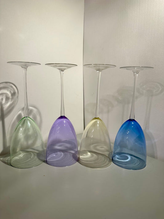 Four colorful wine glasses upside down on a neutral background