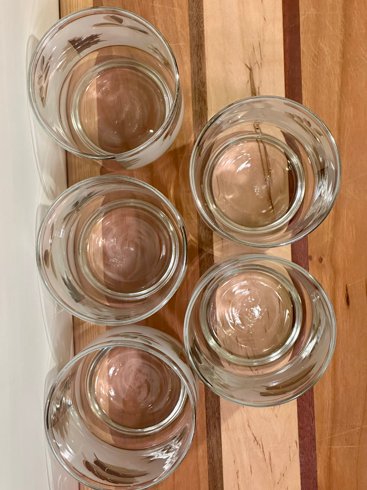 Five clear glass tumblers top view arranged on a striped wooden surface.