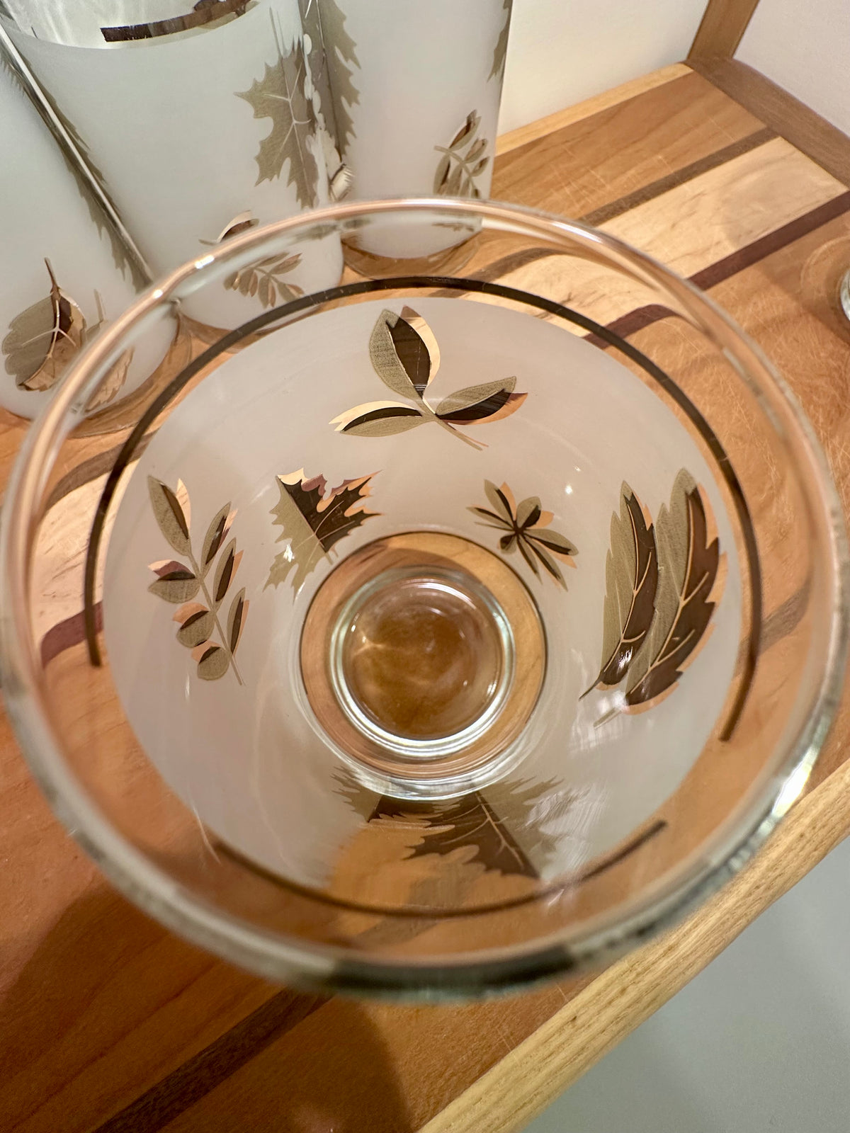 A frosted glass with etched silver leaf patterns, shown from a top-down perspective on a wooden surface.