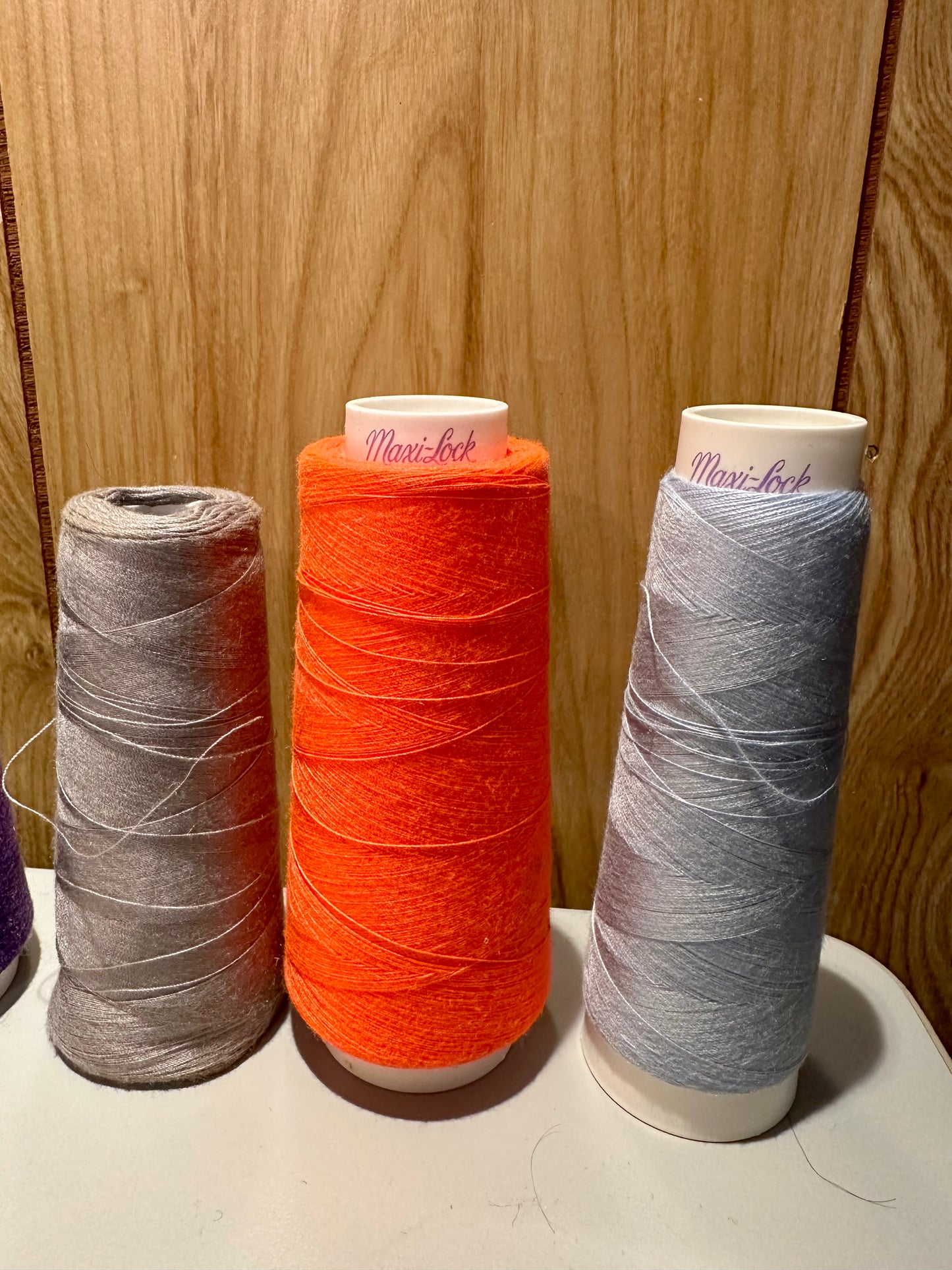 Three spools of thread in gray, orange, and blue on a wooden surface.