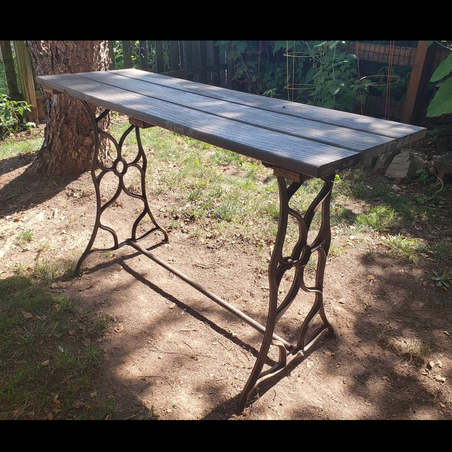 Reclaimed console table made from a cast iron Singer sewing machine base and composite decking, designed as a durable outdoor plant table.