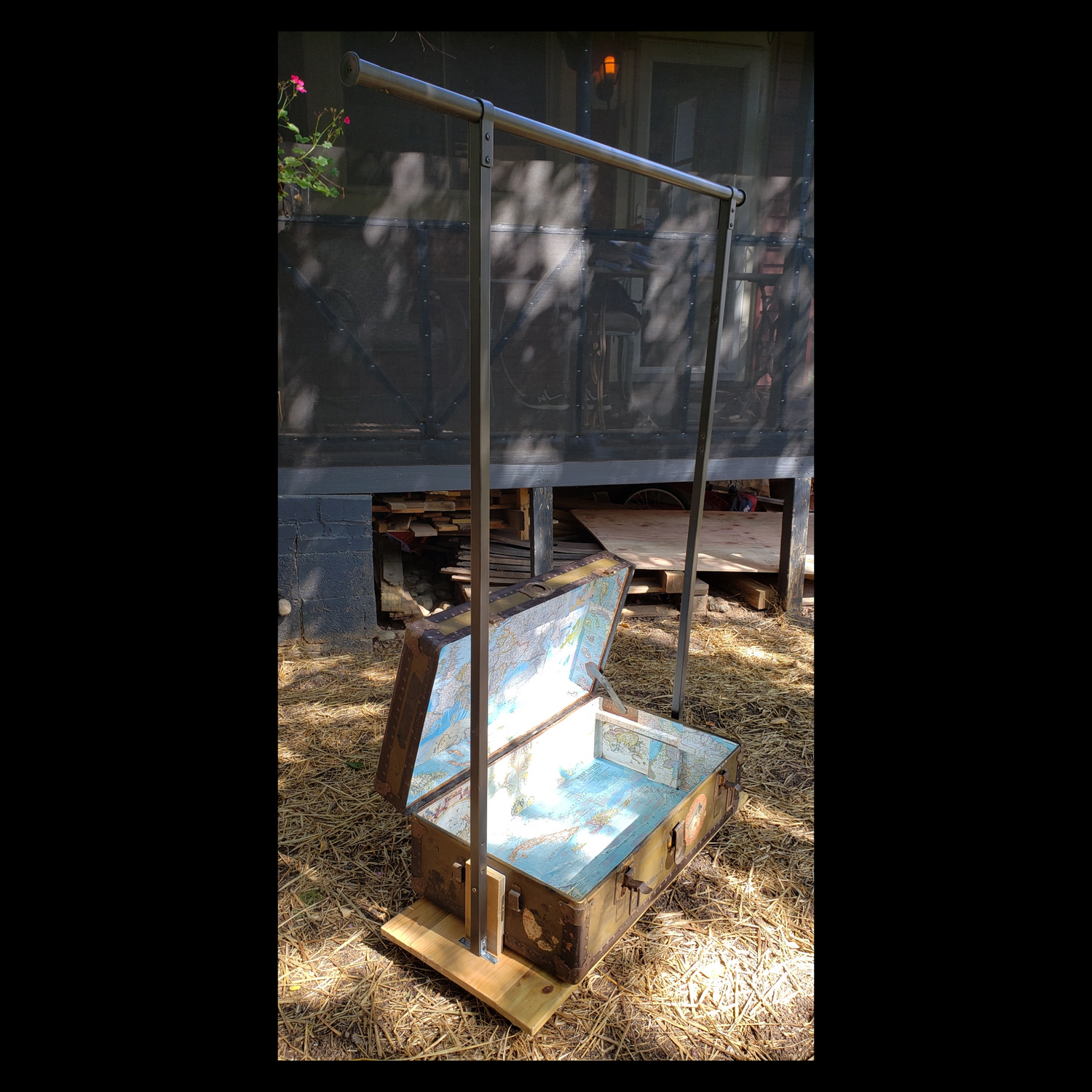Rolling closet made from a vintage steamer trunk mounted on a wheeled platform, featuring a clothing rack and interior lined with vintage maps.