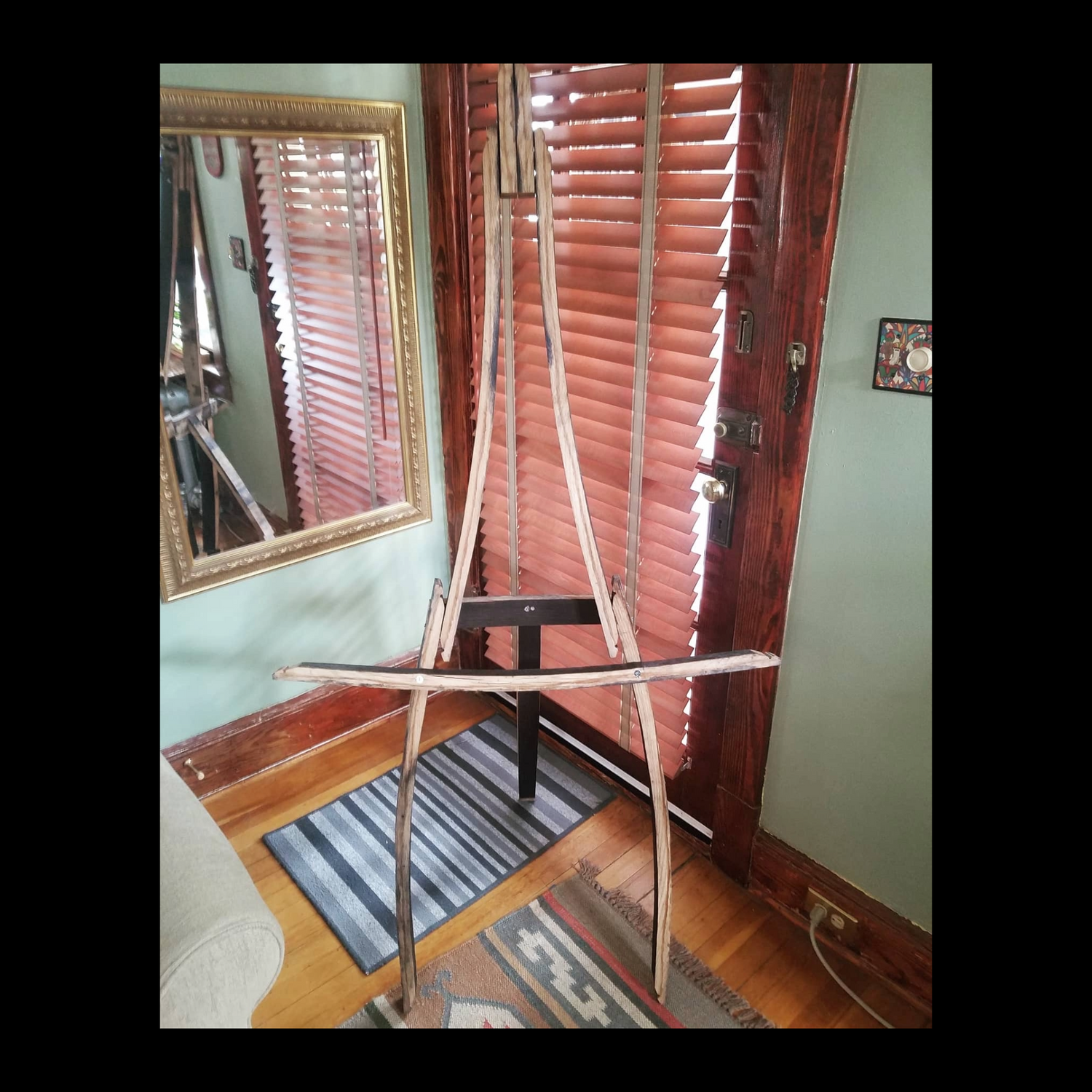 Sturdy barrel stave easel with hinged back leg that folds for space-saving, designed to hold large, heavy framed art.