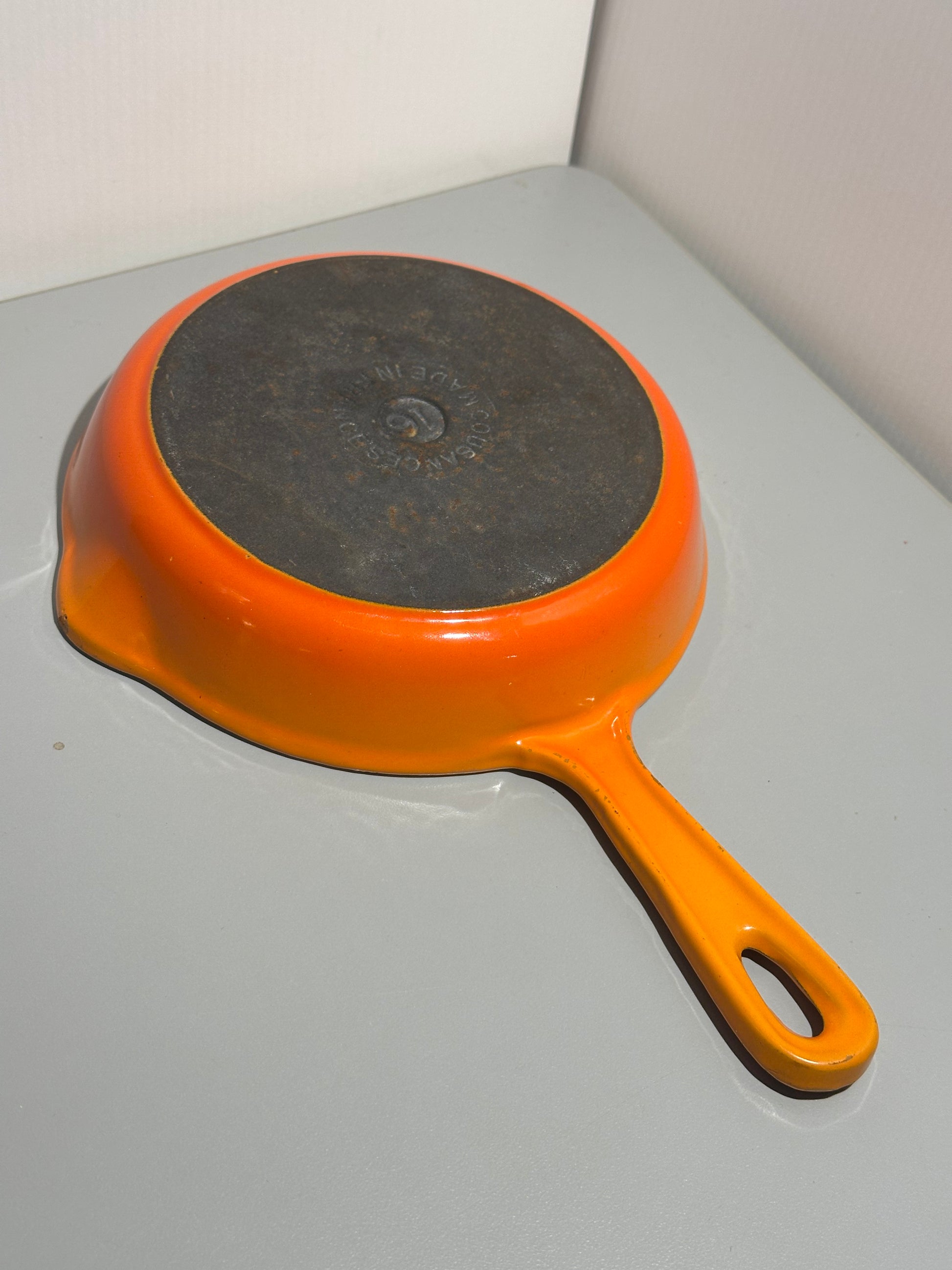 Orange frying pan with black bottom on a light gray surface