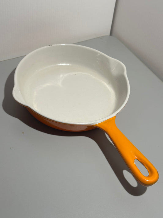 White cast iron skillet with orange handle on a gray surface