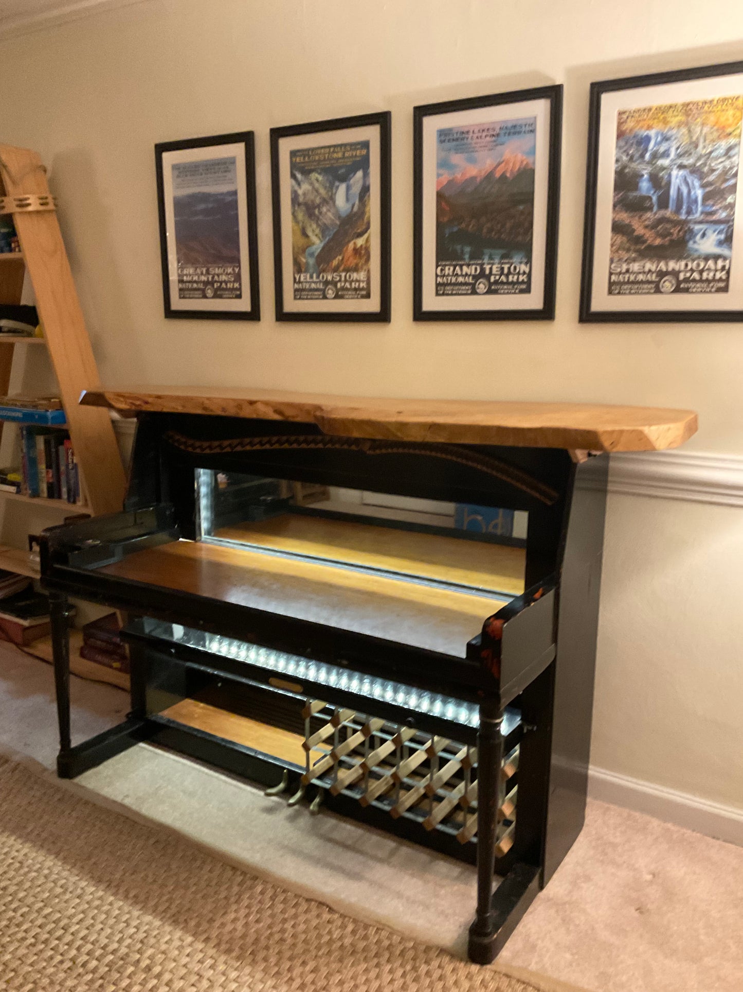 Wine rack with open door displaying bottles against a wall with framed pictures.