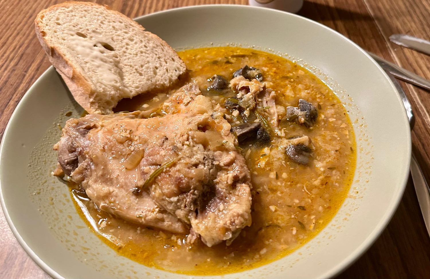 Bowl of cooked rabbit and snail stew with bread on a wooden table