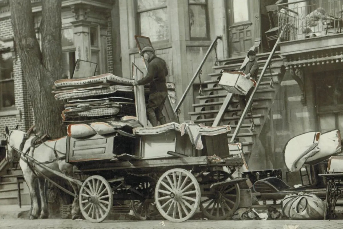 Black and white photo from the 1920s of a horse drawn wagon on moving day with furniture, trunks, and household items being packed to be moved.