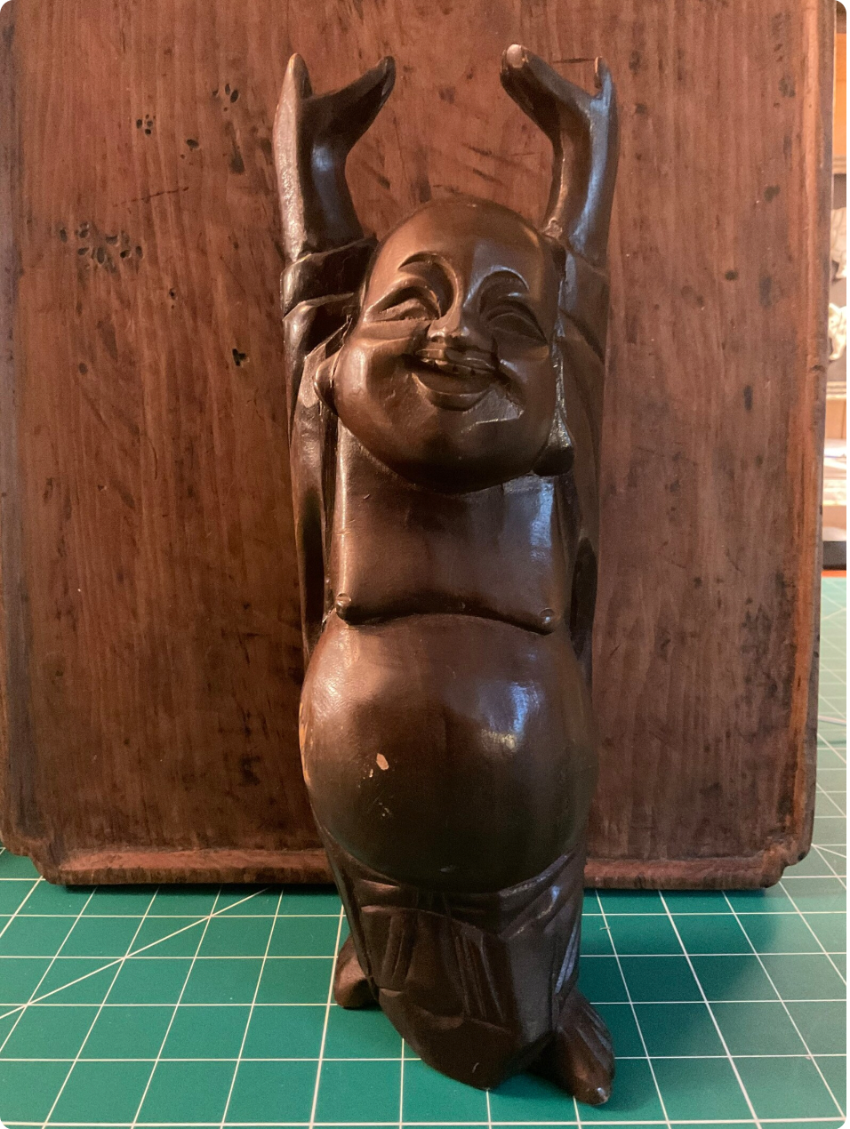 Wooden figurine of a smiling Buddah on a grid surface.