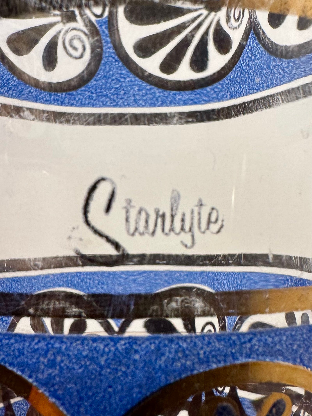 Close-up of a decorative glass surface with blue and gold ornamental patterns and the handwritten name 'Starlyte' in  script across the center.