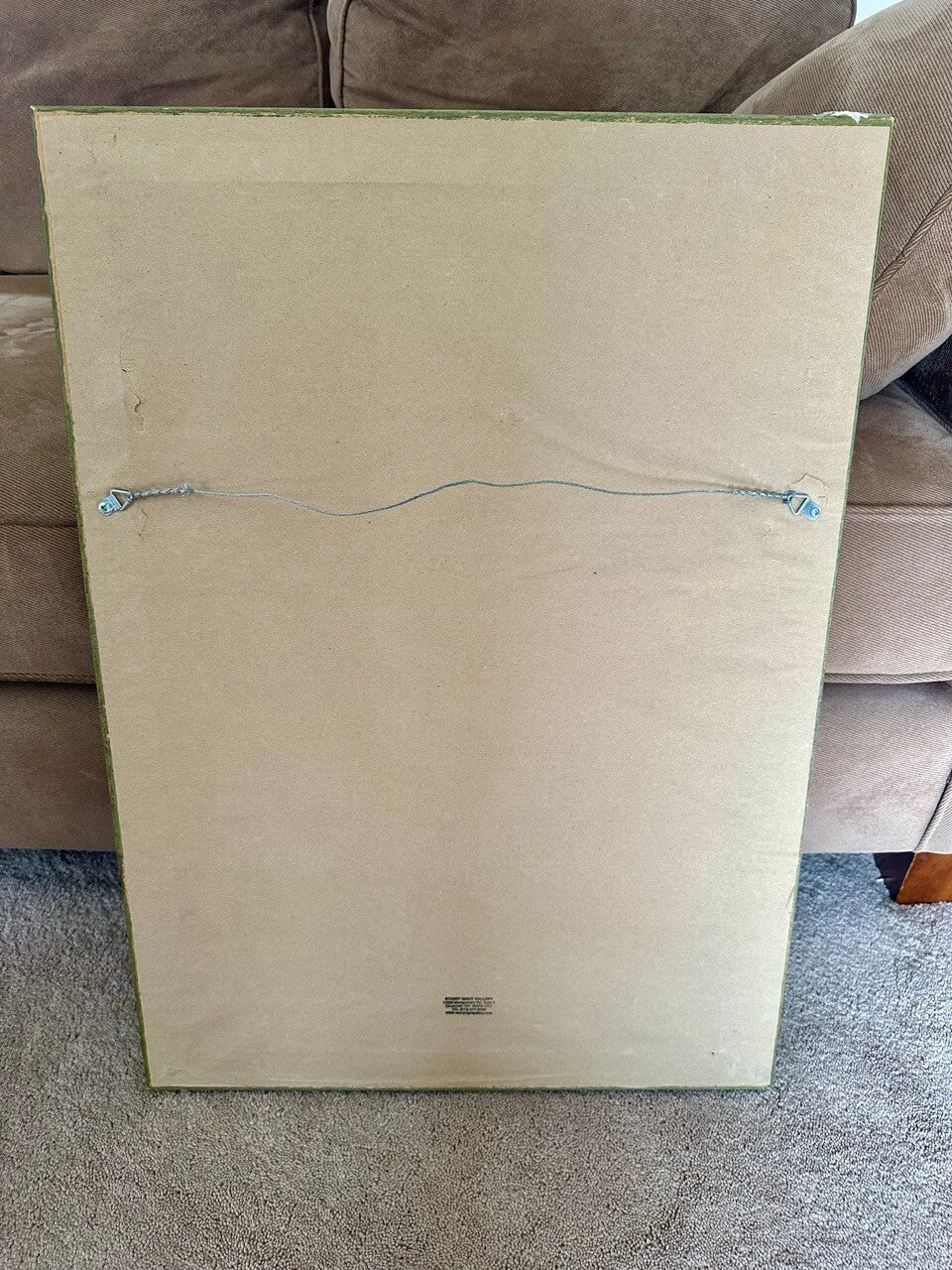 Dust cover side of a framed picture on a carpeted floor with a brown couch in the background