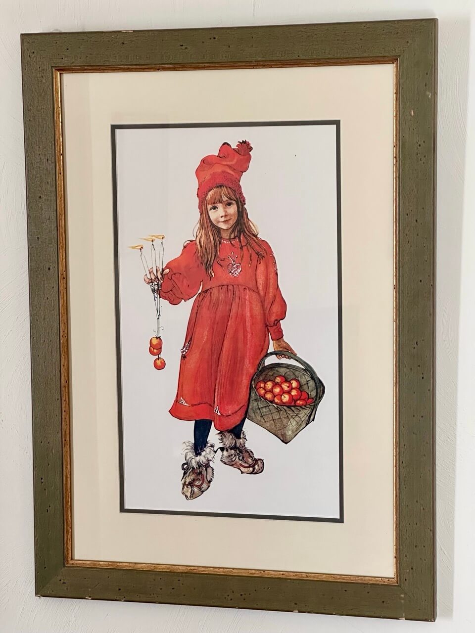Framed illustration of a girl in a red outfit holding apples.