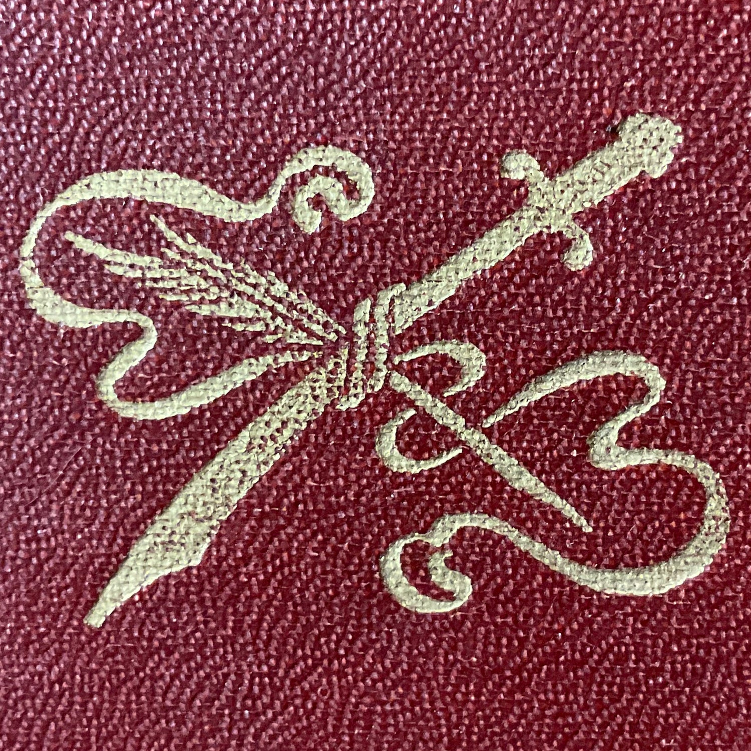 A sword crossing a feather pen, with scrolled ribbon binding the two together. Gold on red.