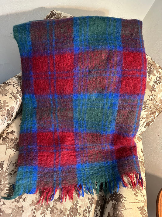 Plaid blanket with red, blue, and green colors draped over a textured surface.