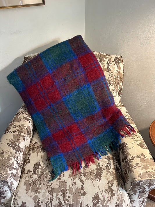Plaid blanket draped over a floral-patterned chair against a plain wall.