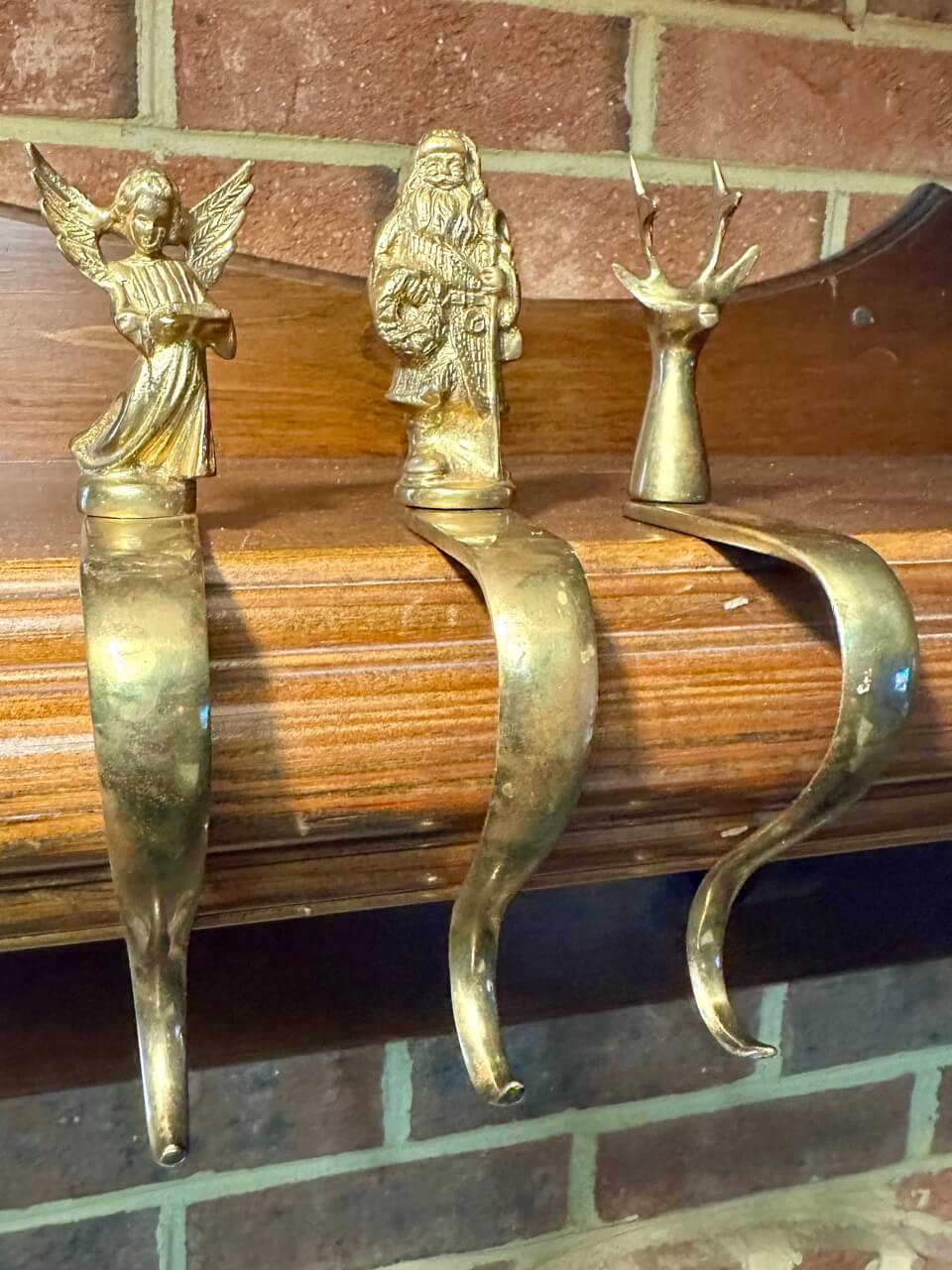Three brass stocking hooks on a mantelpiece with brick background.