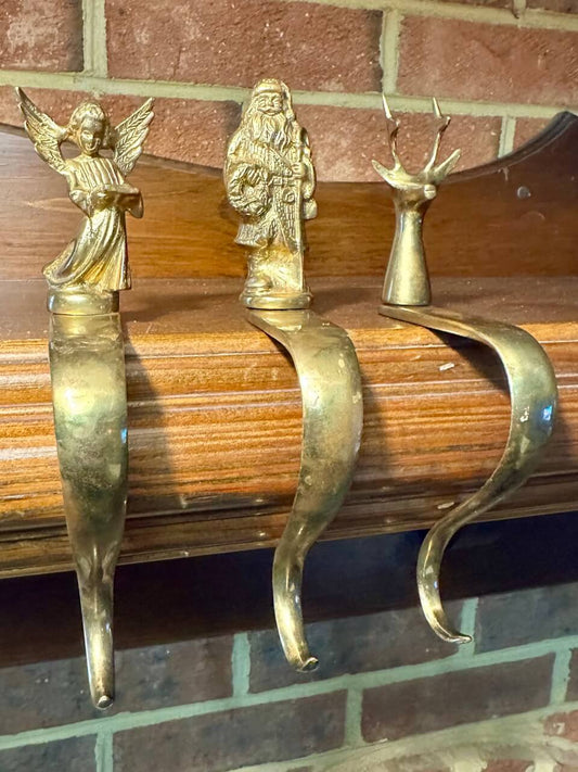 Three brass stocking hooks on a mantelpiece with brick background.