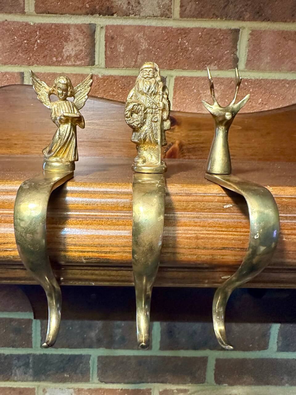 Three brass stocking hooks - an angel, father christmas, and a reindeer on a mantel.