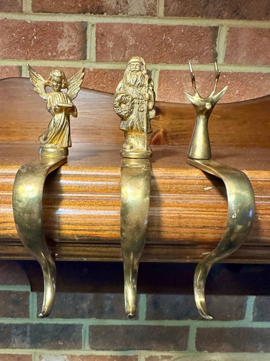Three brass stocking hooks - an angel, father christmas, and a reindeer on a mantel.