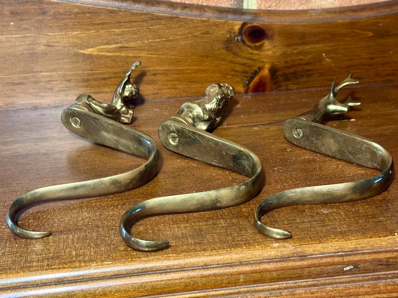 3 brass stocking hangers laying on their side on a wooden surface.