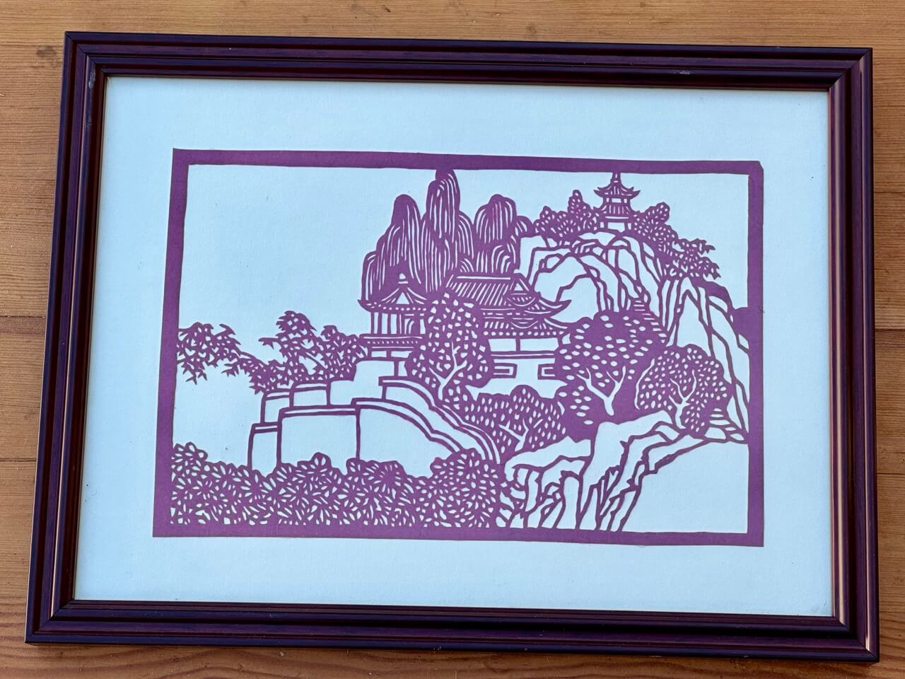 Japanese paper cutting stencil of a building on a wooded hillside.