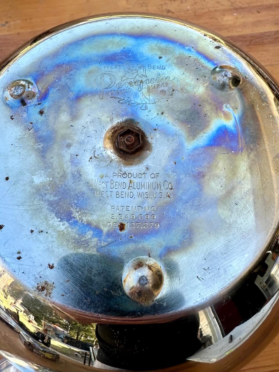 Metallic object with 'West Bend Aluminum Co' branding on a wooden surface